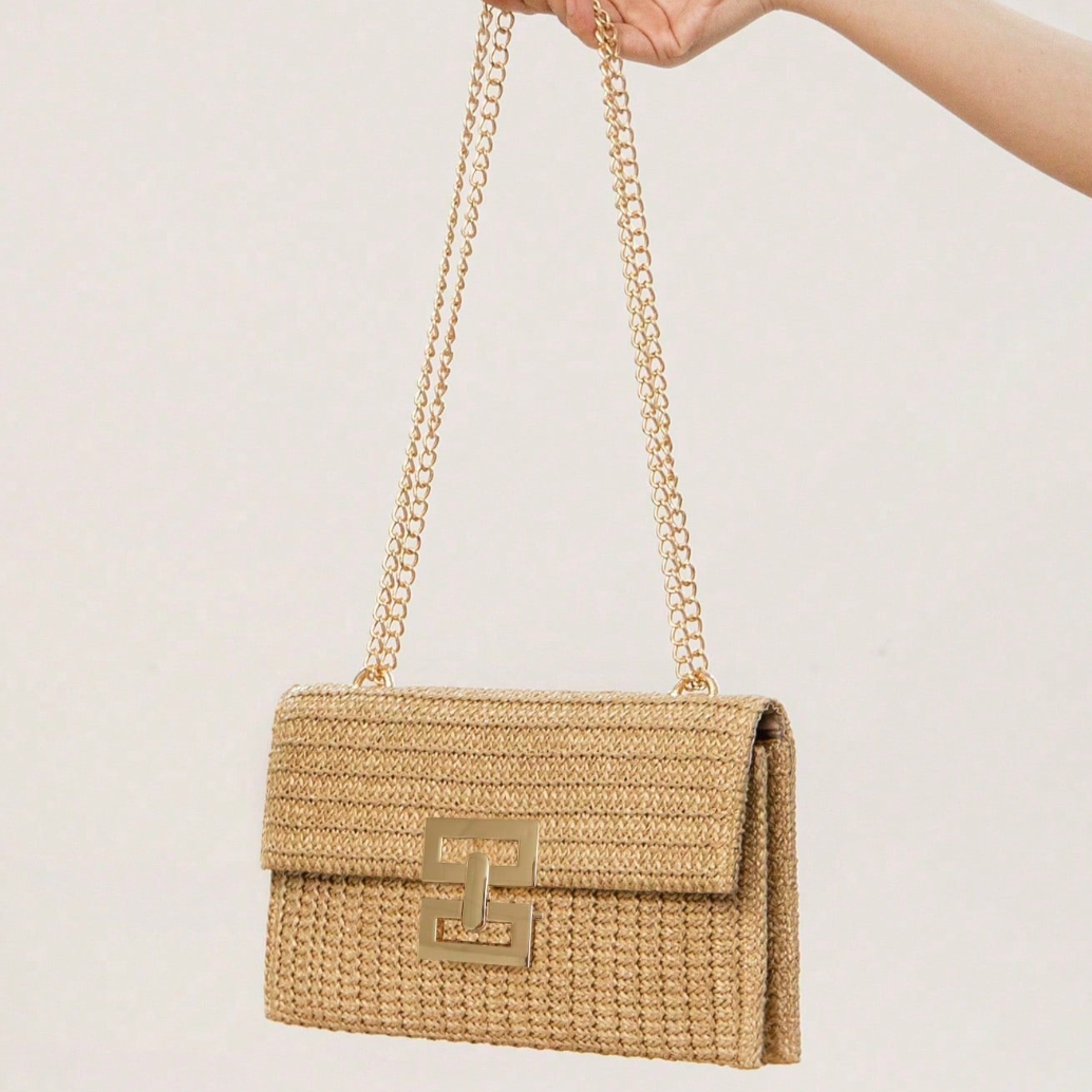 Hand holding a woven handbag with a gold chain strap against a light background