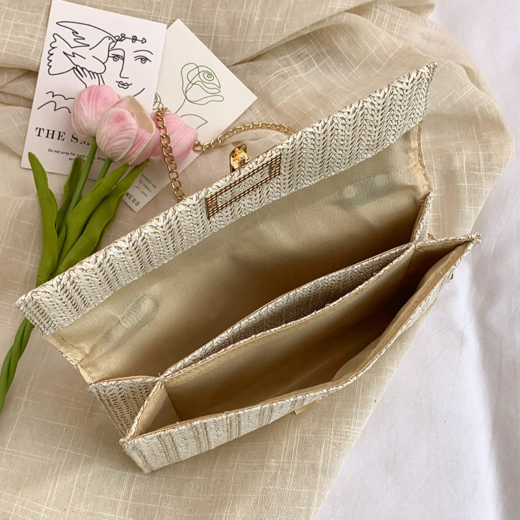 Open beige clutch bag with flowers and jewelry on a textured surface