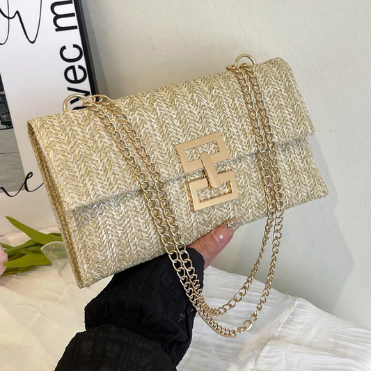 Gold handbag with chain detail held by a hand against a light background